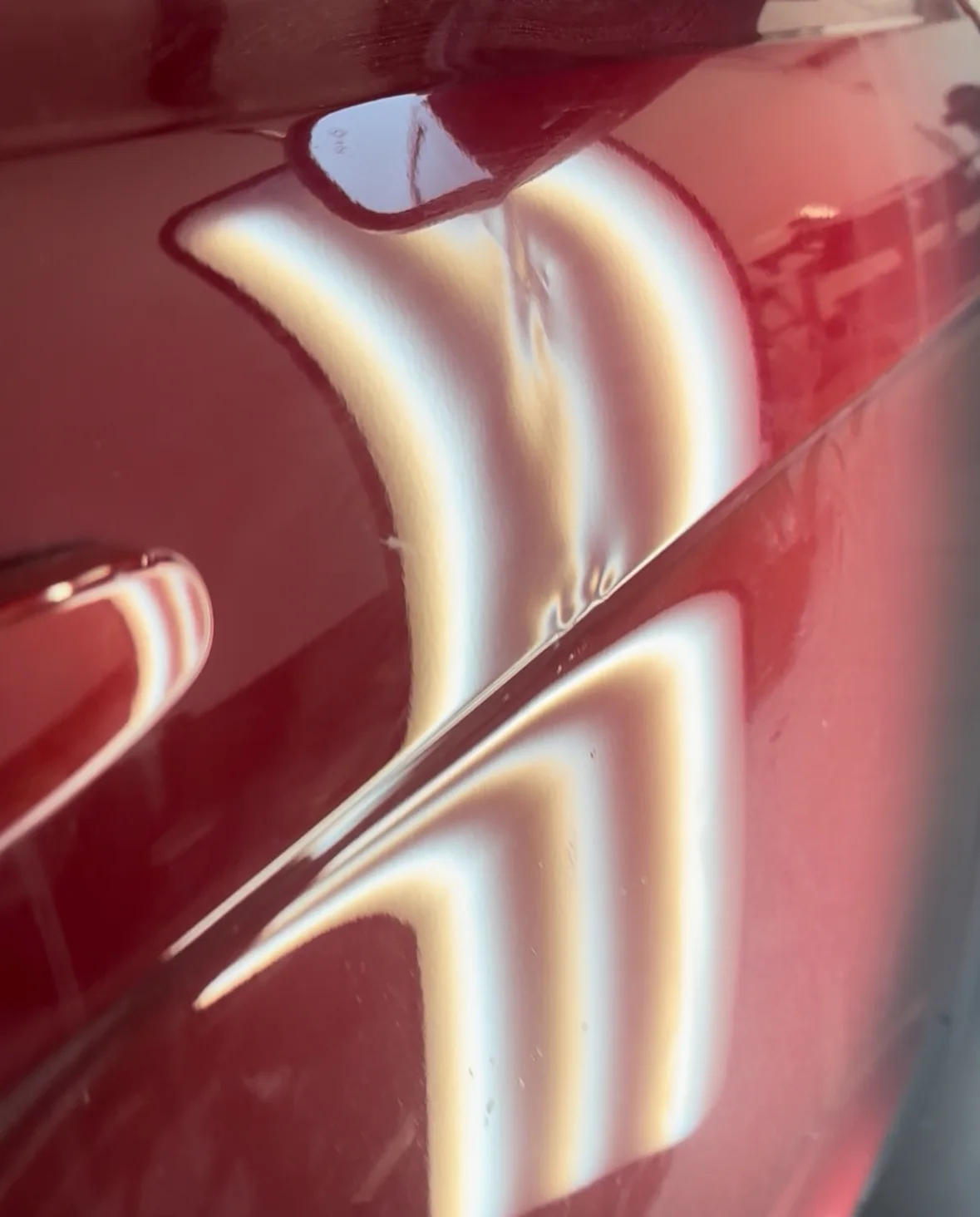 Before repair: reflection lines bending through a dent in a red vehicle door