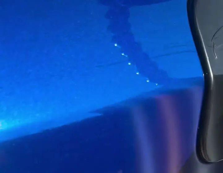A blue vehicle panel showing a dent under inspection lighting